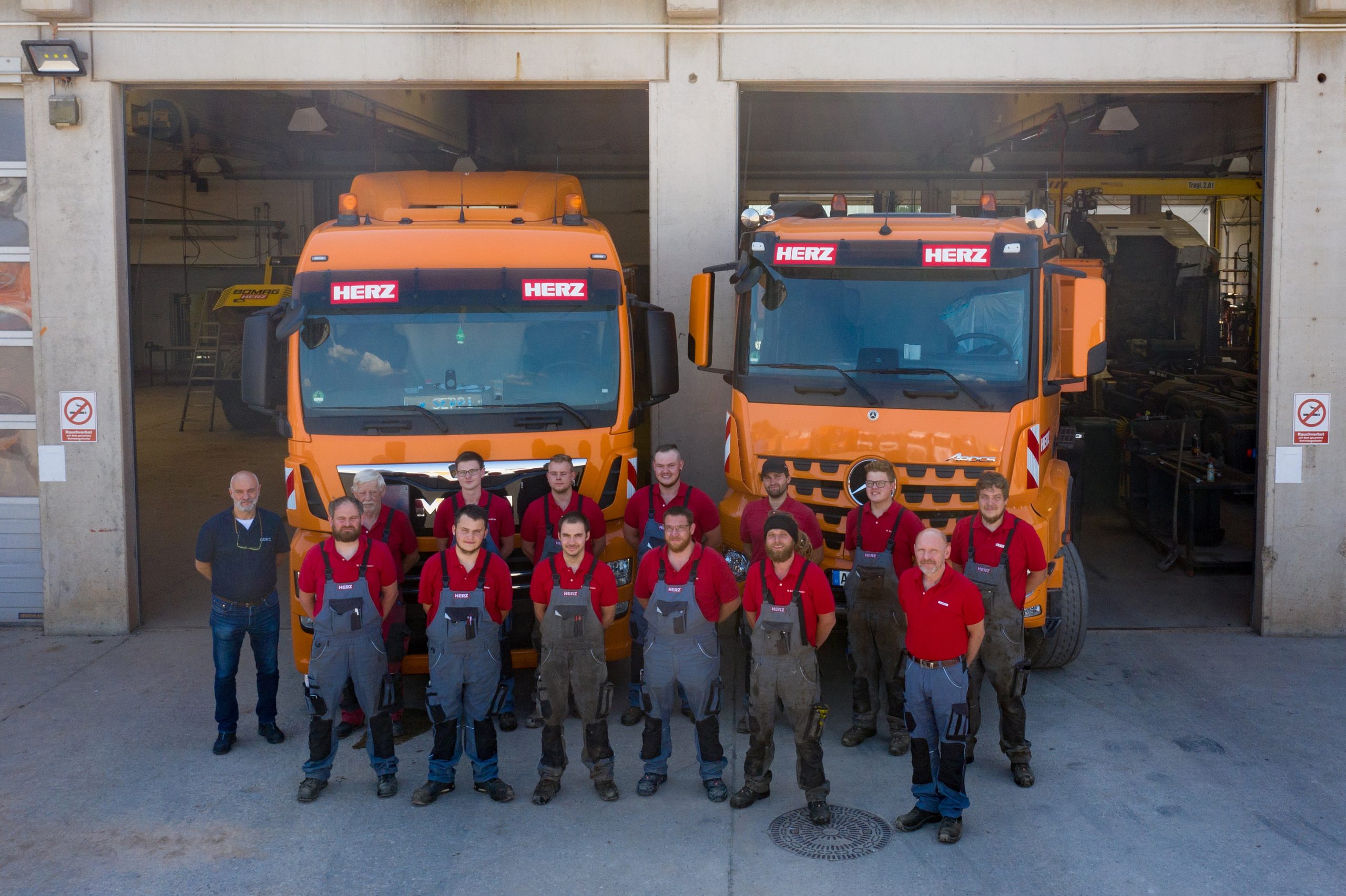 Das HERZ-Werkstattteam mit über 13 Mitarbeitenden vor zwei neuen großen Erdbau-LKW. 
